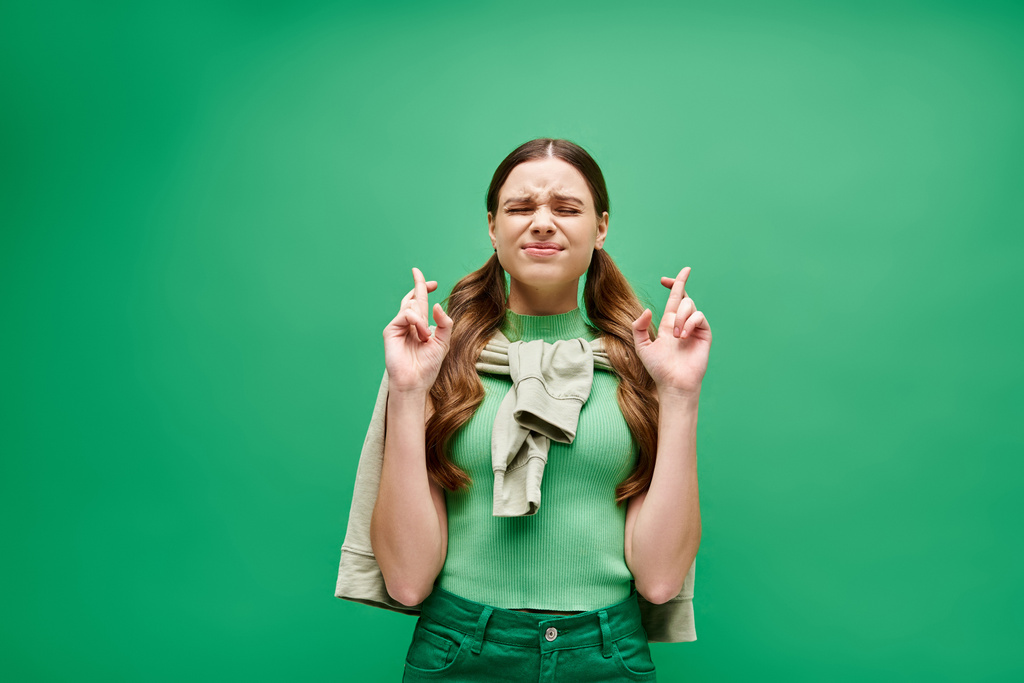 20 'li yaşlarda genç bir kadın yeşil bir arka planla stüdyo ortamında parmaklarıyla yüzünü çaprazladı.. - Fotoğraf, Görsel