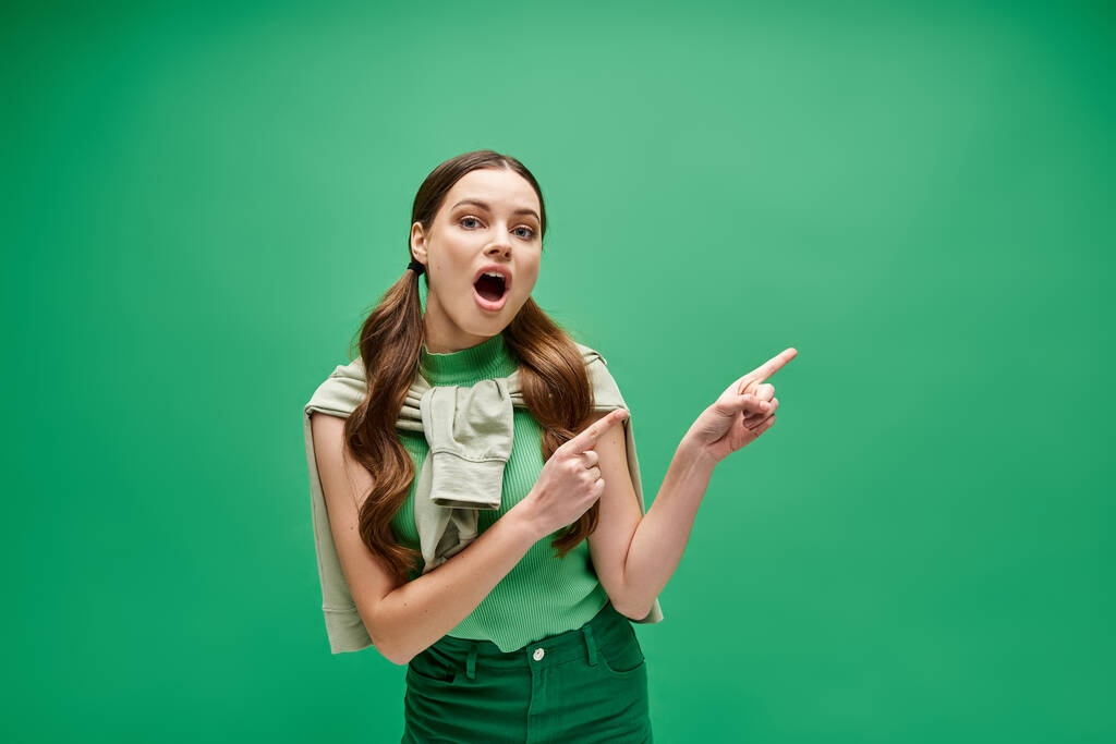 Молода жінка в 20 років, одягнена в зелену сорочку, вказує на щось поза екраном з цікавим виразом. - Фото, зображення