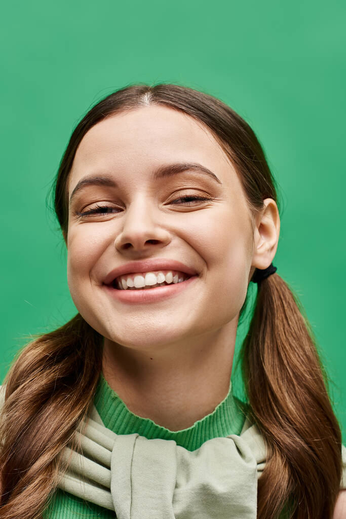 Une jeune femme d'une vingtaine d'années aux cheveux longs habille élégamment une chemise verte avec pull en studio. - Photo, image