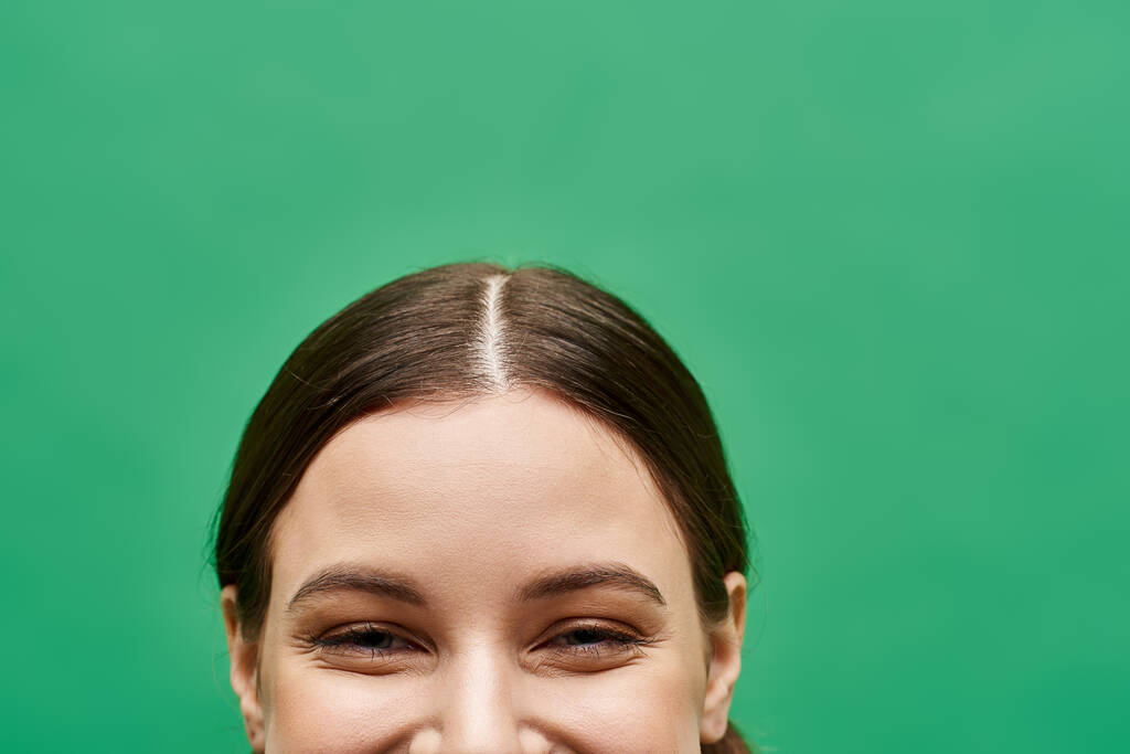 Молодая женщина в возрасте 20 лет, излучающая радость очаровательными улыбающимися глазами в студии с зеленым фоном. - Фото, изображение