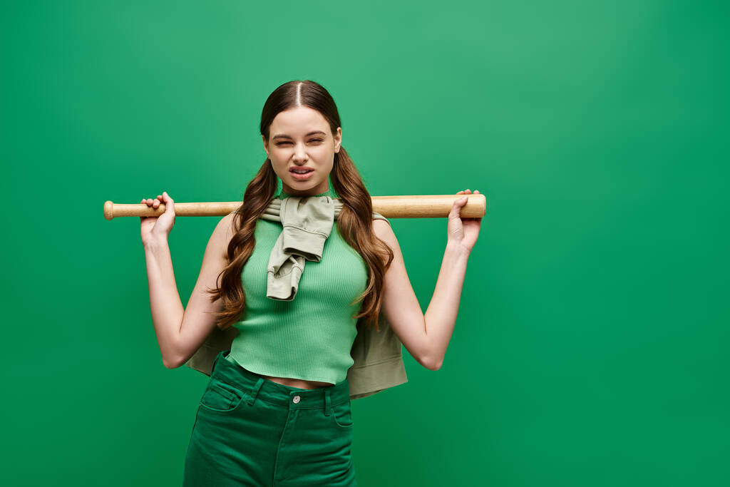 Uma jovem mulher bonita na casa dos 20 anos segura um taco de beisebol sobre o ombro em um estúdio em um fundo verde. - Foto, Imagem