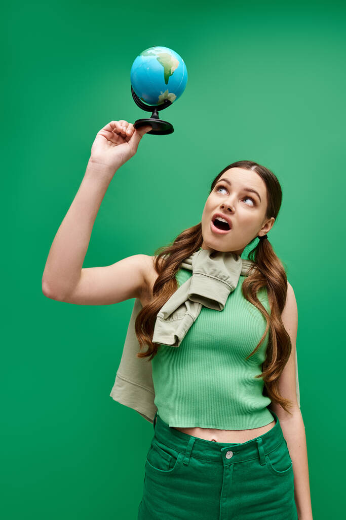 Μια νεαρή όμορφη γυναίκα, γύρω στα 20, φορώντας πράσινο πουκάμισο, κρατώντας μια μπλε σφαίρα σε ένα στούντιο.. - Φωτογραφία, εικόνα