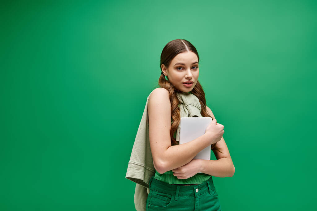 Oszałamiająca, młoda kobieta po dwudziestce, ubrana w zieloną koszulę, trzyma tablet w urzekającym studio.. - Zdjęcie, obraz