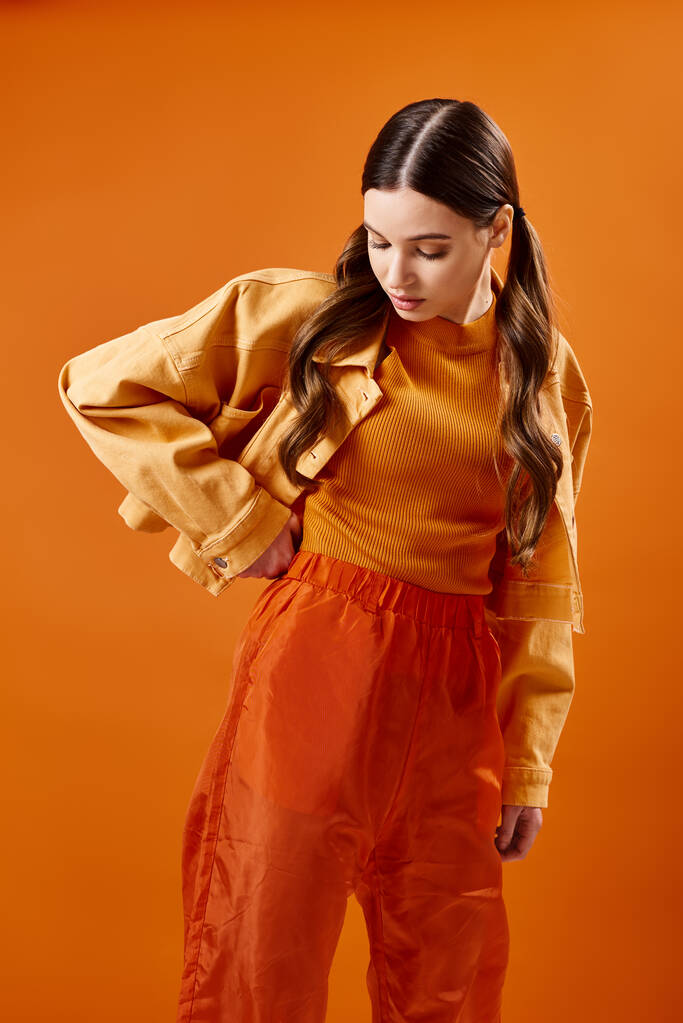 20 'li yaşlarda şık genç bir kadın canlı turuncu bir arka planın önünde zarif bir şekilde duruyor, zarafet ve duruş yayıyor.. - Fotoğraf, Görsel
