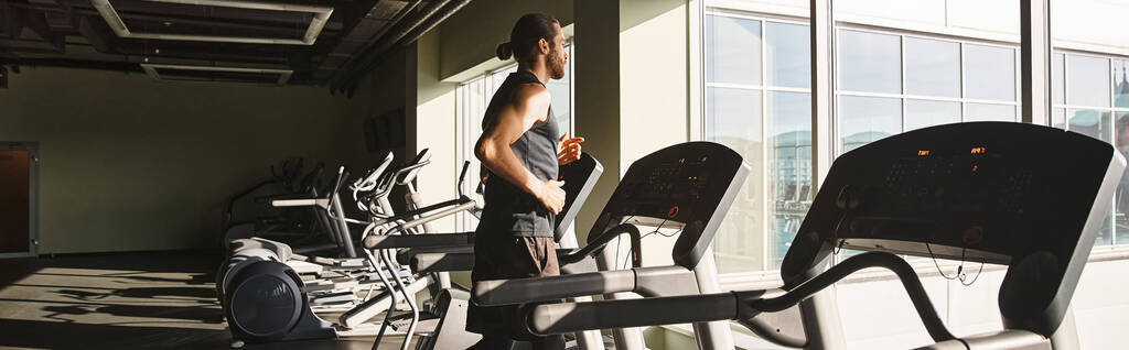 Um homem em forma no desgaste atlético está ao lado de uma fileira de bicicletas de exercício em um ginásio. - Foto, Imagem