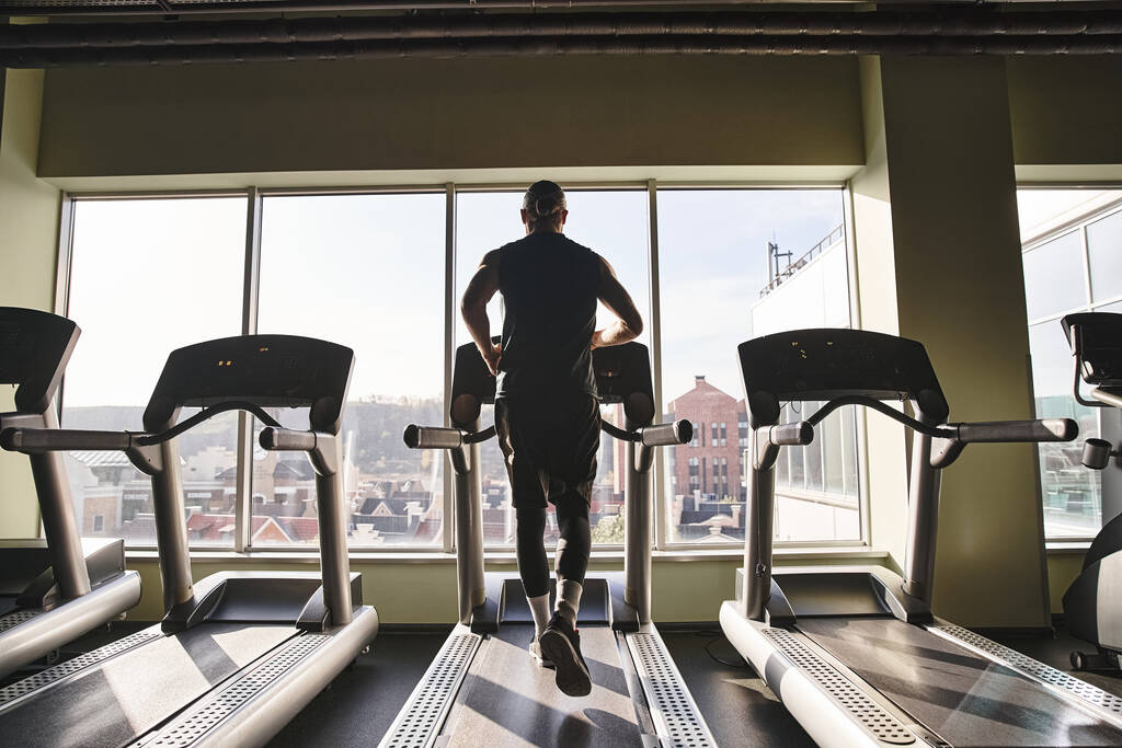 Здоровый человек в спортивной одежде бегает по беговой дорожке в спортзале, прикладывая усилия и энергию к тренировкам.. - Фото, изображение