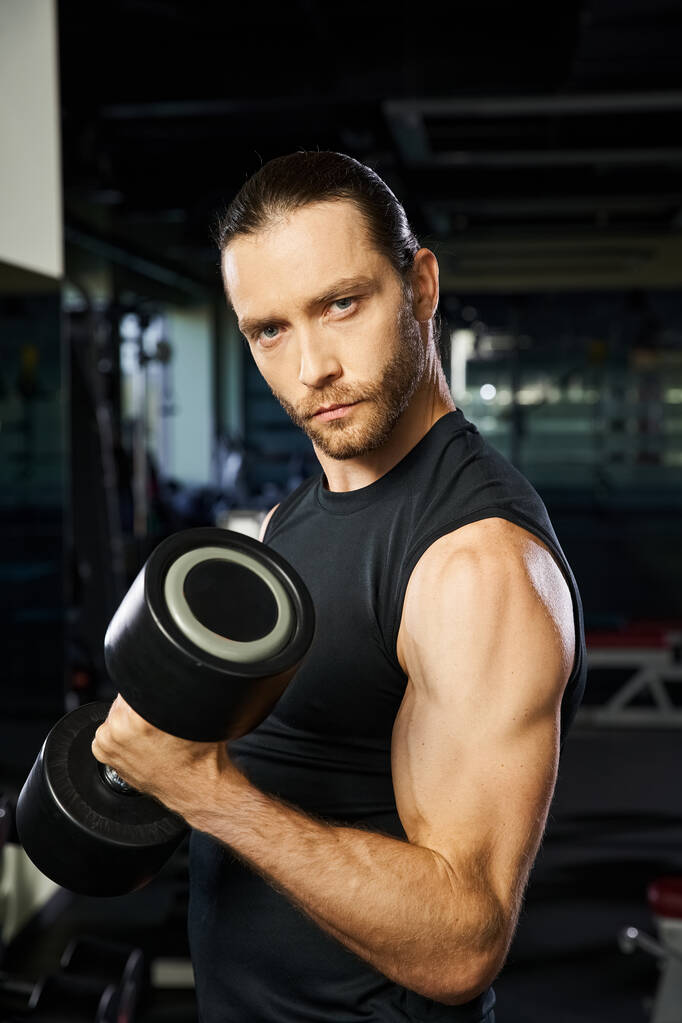 Un homme en tenue active tient un haltère dans une salle de gym, montrant son athlétisme et son dévouement à la forme physique. - Photo, image