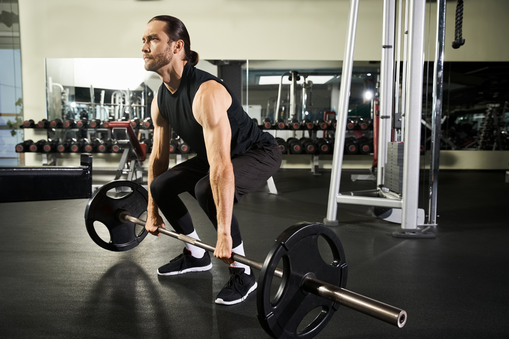 Ein athletischer Mann in aktiver Kleidung hebt in einem Fitnessstudio eine Langhantel und demonstriert Stärke und Entschlossenheit. - Foto, Bild