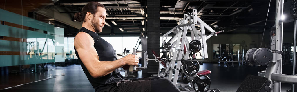 Hombre atlético en desgaste activo que participa en una rutina de entrenamiento utilizando una máquina en un gimnasio. - Foto, Imagen