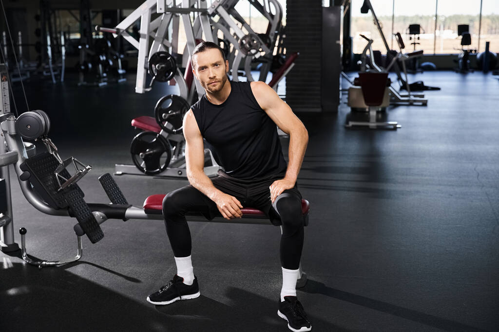 Ein athletischer Mann in aktiver Kleidung sitzt auf einer Gymnastikbank und überlegt kurz über seine Fitness-Reise nach. - Foto, Bild