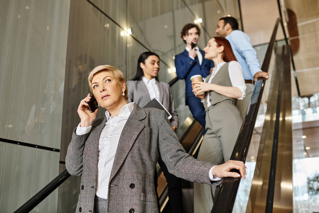 Una mujer de negocios en acción, hablando en un teléfono celular mientras está de pie en una escalera mecánica en movimiento. - Foto, imagen