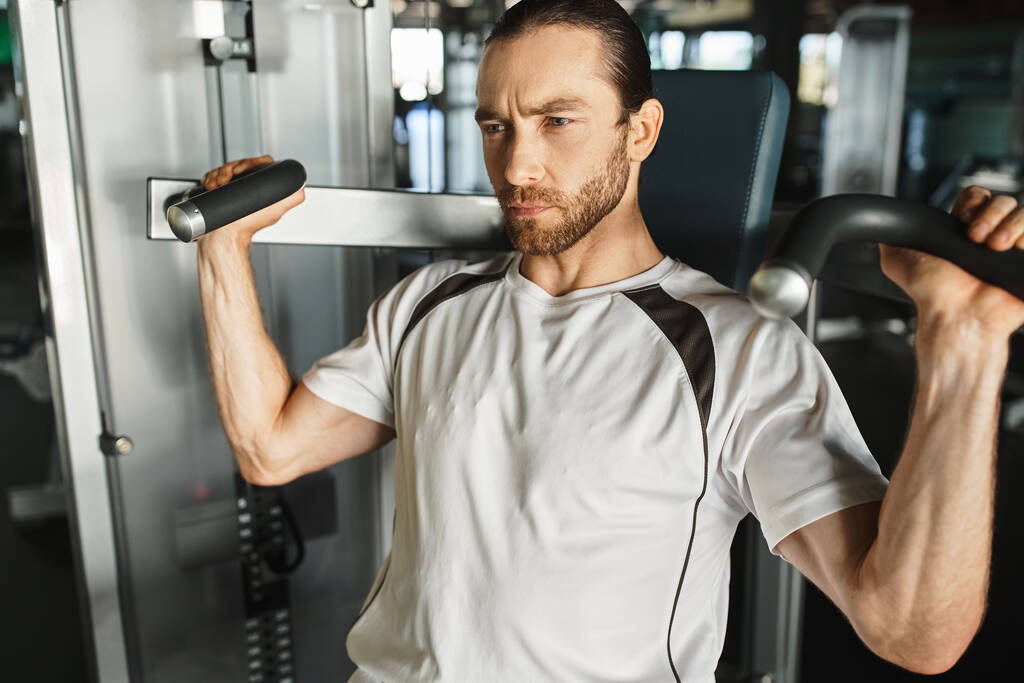 Een atletische man in actieve kleding, met een handvat op een fitnessapparaat tijdens het sporten in de sportschool. - Foto, afbeelding