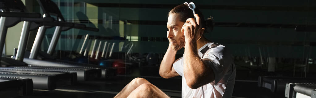 Ein Mann in aktiver Kleidung sitzt auf einer Matte, vertieft in seine Musik - Foto, Bild