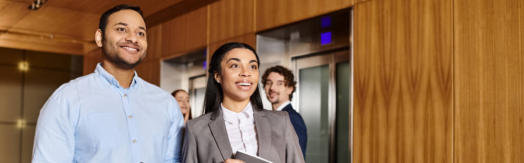 Um homem e uma mulher, um grupo inter-racial de profissionais de negócios, ficam em frente a um elevador. - Foto, Imagem