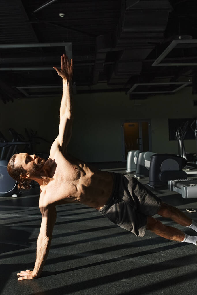 Μυώδης άνθρωπος, χωρίς πουκάμισο, επιδεικνύοντας δύναμη και ισορροπία με την εκτέλεση ενός πάγκου σε ένα γυμναστήριο. - Φωτογραφία, εικόνα