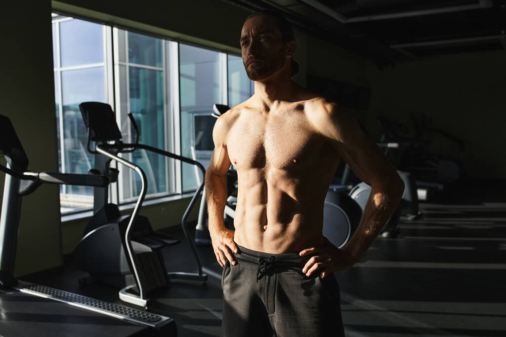 Un uomo muscoloso senza camicia davanti a una macchina da ginnastica, concentrato e pronto all'allenamento. - Foto, immagini