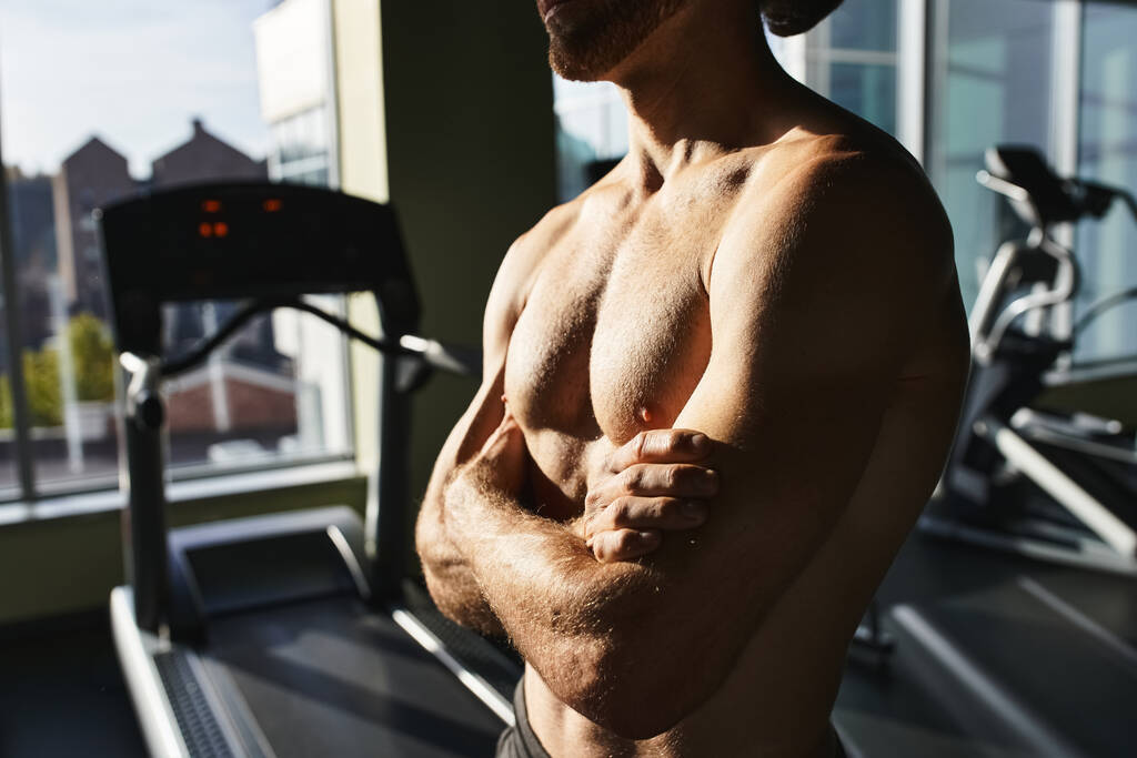 М'язистий чоловік, без сорочки, поруч з біговою доріжкою в спортзалі. - Фото, зображення