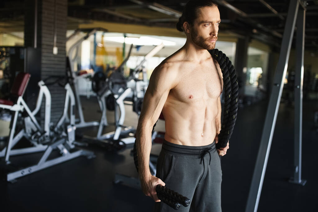Ein muskulöser Mann steht selbstbewusst in einem Fitnessstudio, konzentriert auf sein Workout-Programm und demonstriert seine Hingabe zum Kraftaufbau. - Foto, Bild