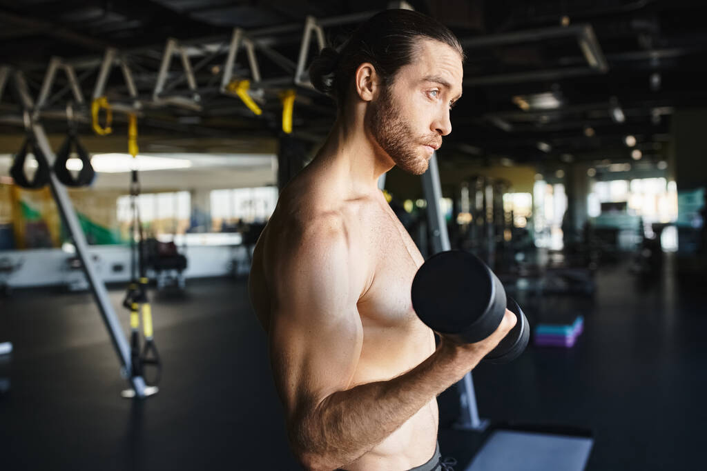 Un uomo senza maglietta in una palestra che tiene un manubrio, mostrando il suo fisico muscolare e la sua dedizione al fitness. - Foto, immagini
