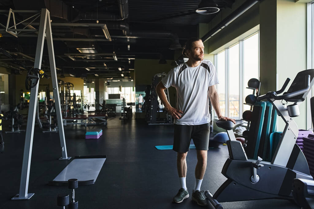 Muskularny mężczyzna stojący w sali gimnastycznej otoczony stojakiem ze sprzętem do ćwiczeń. - Zdjęcie, obraz