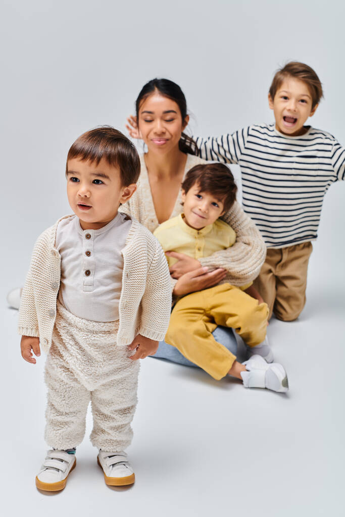 Eine junge asiatische Mutter und ihre Kinder posieren in einem Studio vor grauem Hintergrund. - Foto, Bild