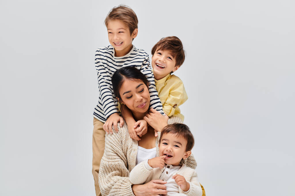 Una giovane madre asiatica e i suoi figli si mettono in posa, trasudando amore e intimità in uno studio sullo sfondo grigio. - Foto, immagini