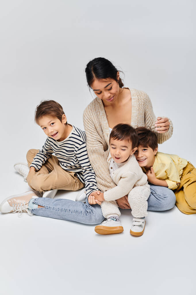 アジアの若い母親が子供たちと地面に座り,家族的な愛とトータルネスシーンを作り出しています.. - 写真・画像