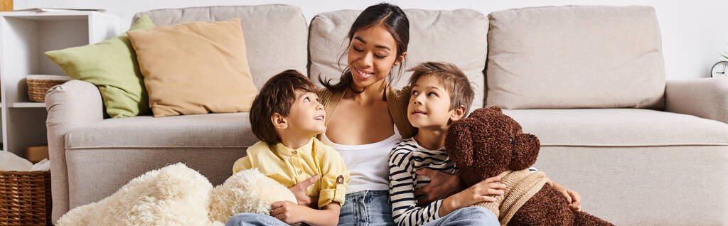 Una joven madre asiática sentada en un sofá con sus dos hijos en una acogedora sala de estar, comprometida en una interacción cálida y amorosa. - Foto, imagen