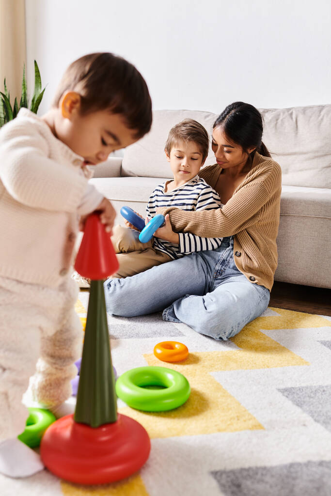 Jovem mãe asiática alegremente se envolve com seus dois filhinhos em brincar e explorar com brinquedos na acolhedora sala de estar. - Foto, Imagem