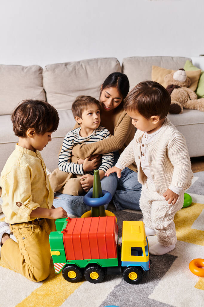 uma jovem mãe asiática e seus filhinhos, brincando energeticamente junto com um caminhão de brinquedo em sua sala de estar. - Foto, Imagem