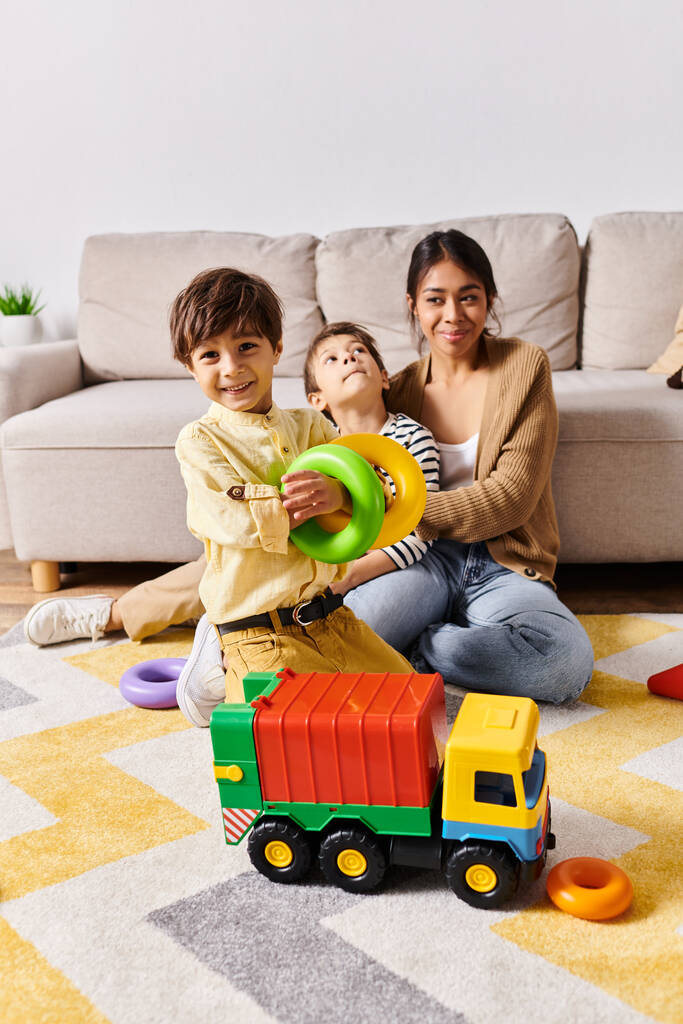 Una giovane madre asiatica e i suoi due piccoli figli giocano felicemente con un camion giocattolo nel loro salotto. - Foto, immagini