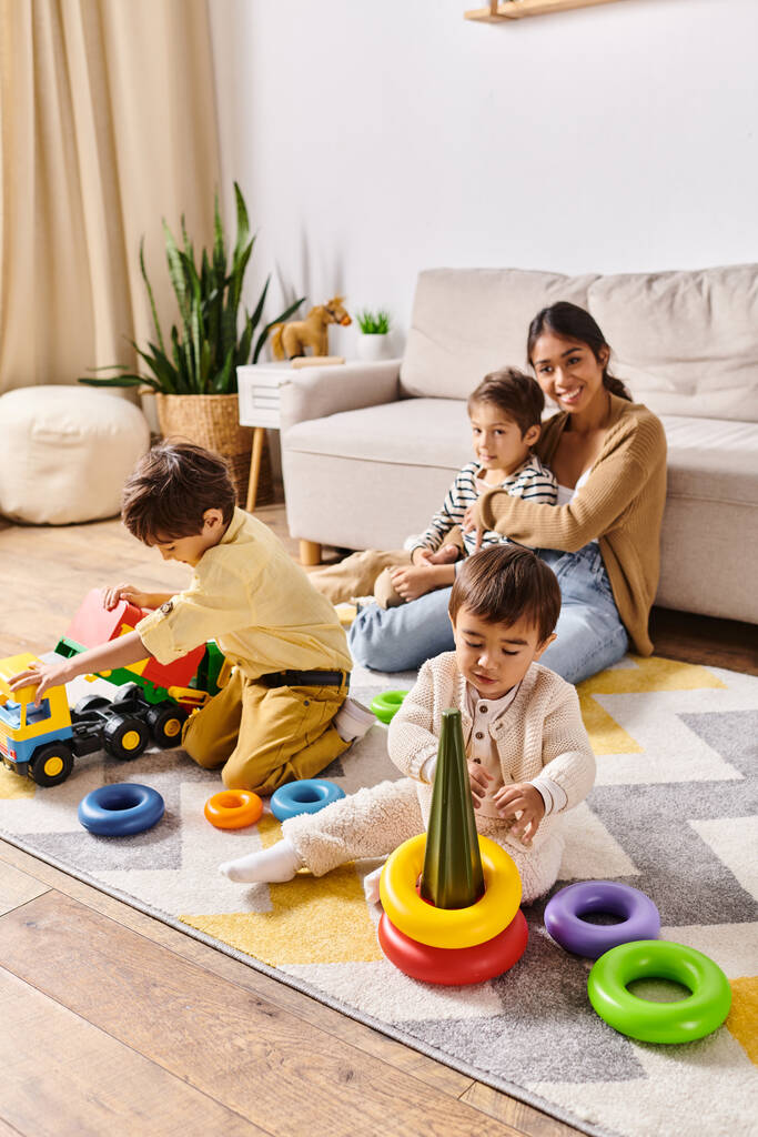 Eine junge asiatische Mutter beobachtet, wie ihre kleinen Söhne in einem warmen, einladenden Wohnzimmer mit bunten Spielzeugen spielen. - Foto, Bild