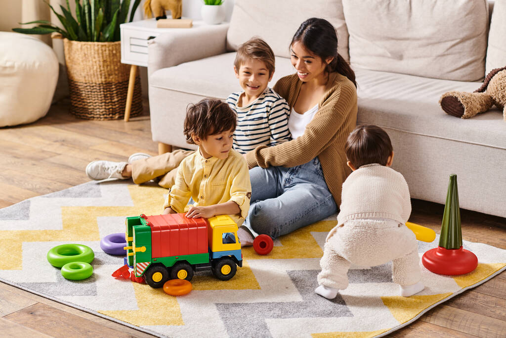 A young Asian mother joyfully sits on the floor, playing with her two little sons in their cozy living room. - Photo, Image
