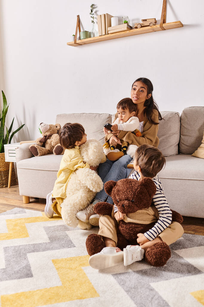 Young Asian mother relaxes on couch surrounded by various stuffed animals while bonding with her little sons in cozy living room. - Photo, Image