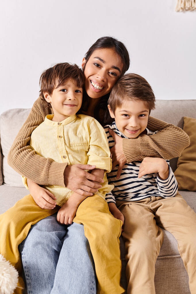 Una joven madre asiática se sienta en un sofá, rodeada de sus dos hijos energéticos, en su acogedora sala de estar en casa. - Foto, imagen
