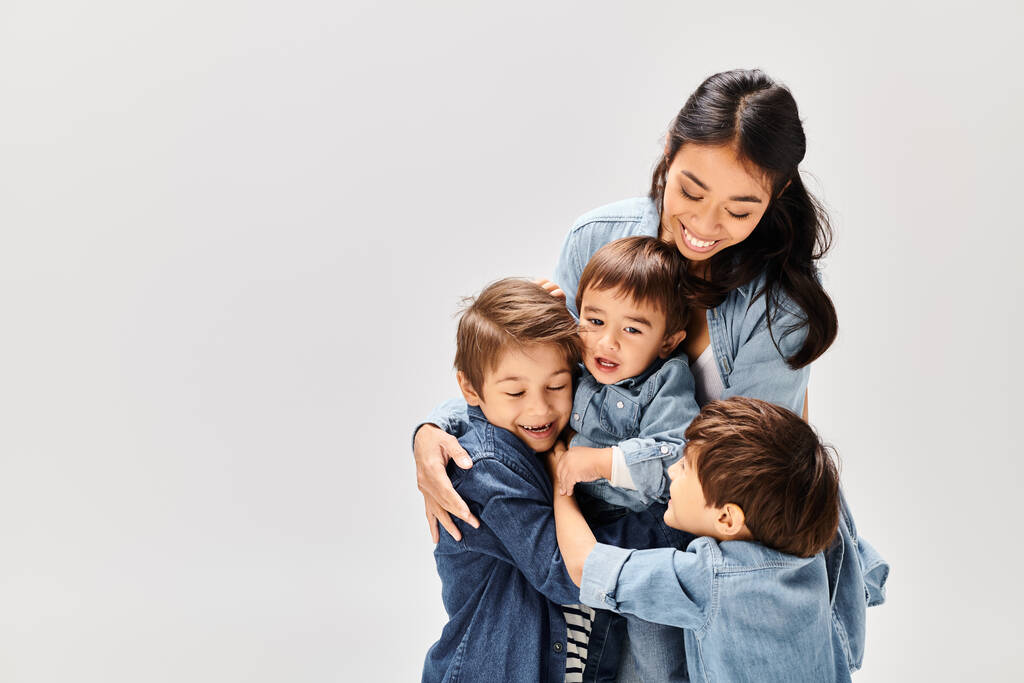 Una giovane madre asiatica abbraccia i suoi due piccoli figli, tutti vestiti in denim, creando un commovente momento di amore e connessione. - Foto, immagini