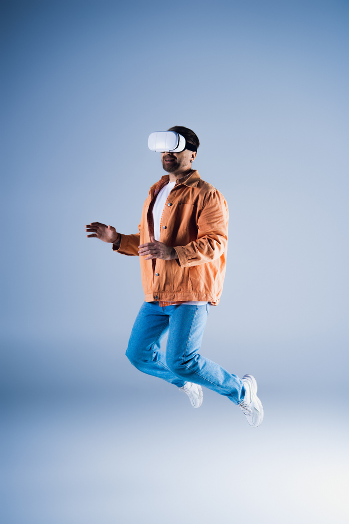 Een man met een hoed springt in de lucht in een studio terwijl hij een VR-headset draagt voor metaverse verkenning. - Foto, afbeelding
