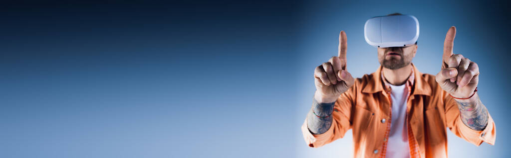 Een man in een oranje jasje staat in een studio, houdt twee vingers omhoog in een gebaar van vrede en eenheid.. - Foto, afbeelding