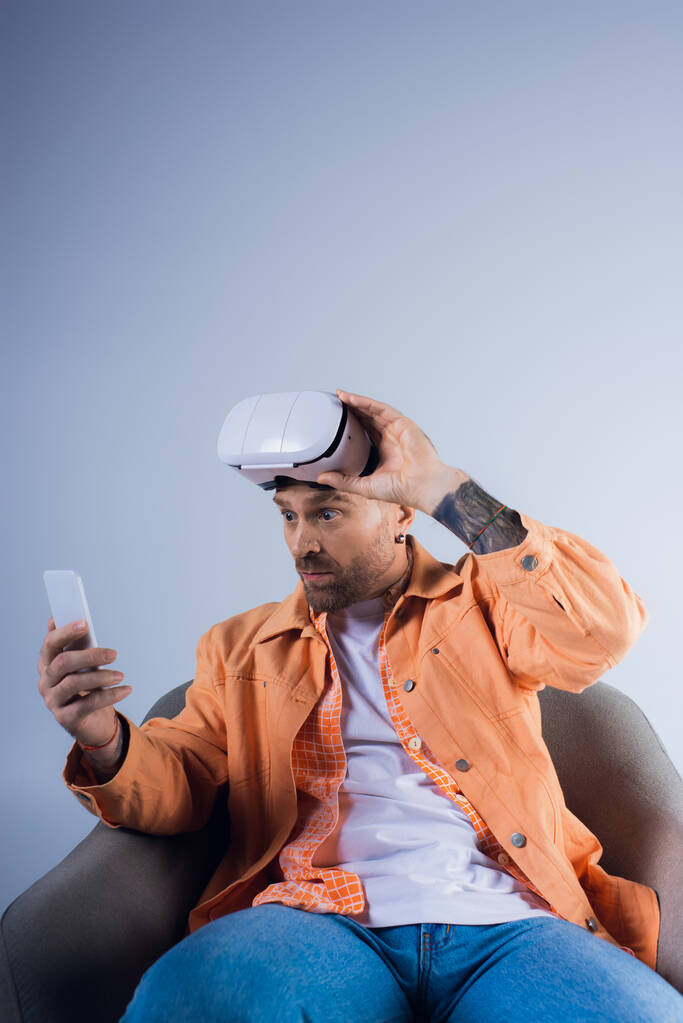 Een man ondergedompeld in de virtuele wereld, zittend in een stoel met een mobiele telefoon in de hand. - Foto, afbeelding