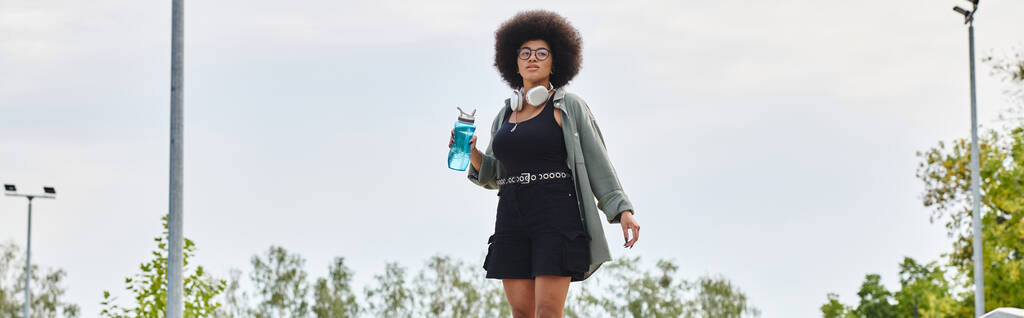 Joven mujer afroamericana con un pelo rizado afro montando un monopatín en un parque de skate. - Foto, imagen