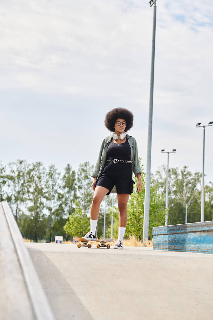 Μια νεαρή Αφροαμερικανή γυναίκα με σγουρά μαλλιά με αυτοπεποίθηση skateboards κάτω από ένα πεζοδρόμιο της πόλης σε μια ηλιόλουστη μέρα. - Φωτογραφία, εικόνα