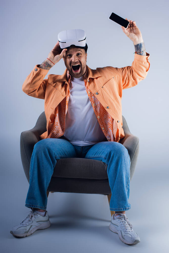 Ένας άντρας κάθεται αναπαυτικά σε μια καρέκλα φορώντας ακουστικά VR, χαμένος στη σκέψη. - Φωτογραφία, εικόνα