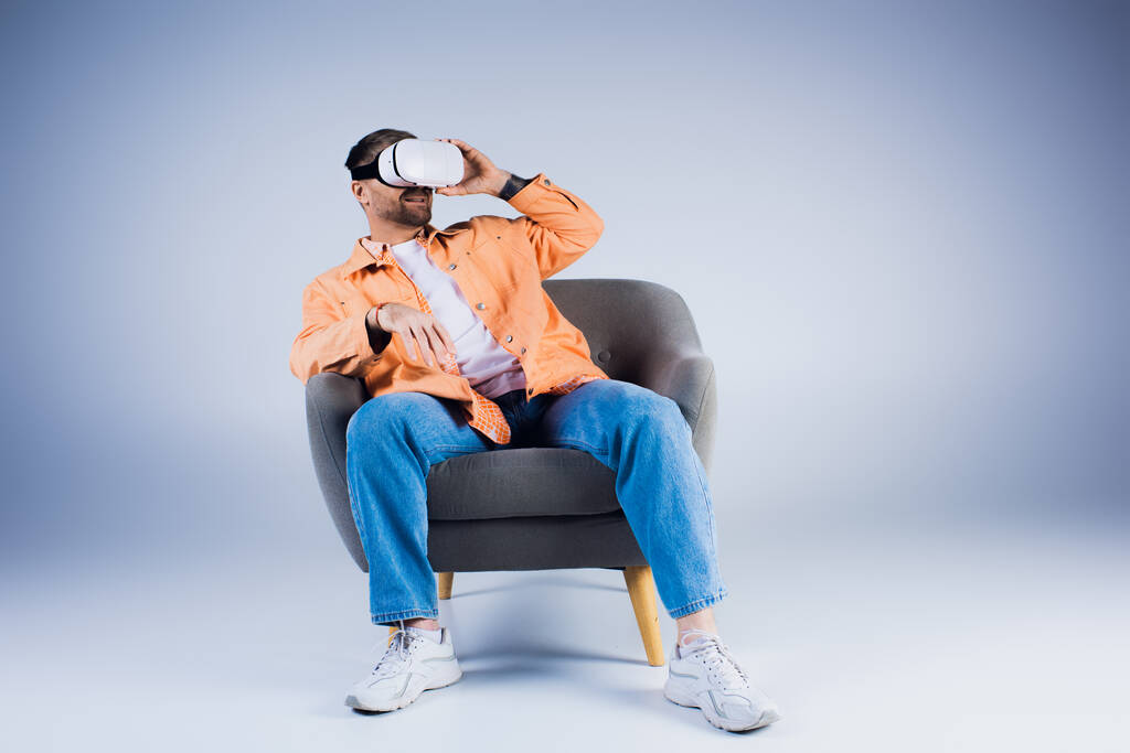 Mies istuu mukavasti tuolissa, käyttää VR-kuulokkeita, eksyksissä studioympäristössä.. - Valokuva, kuva