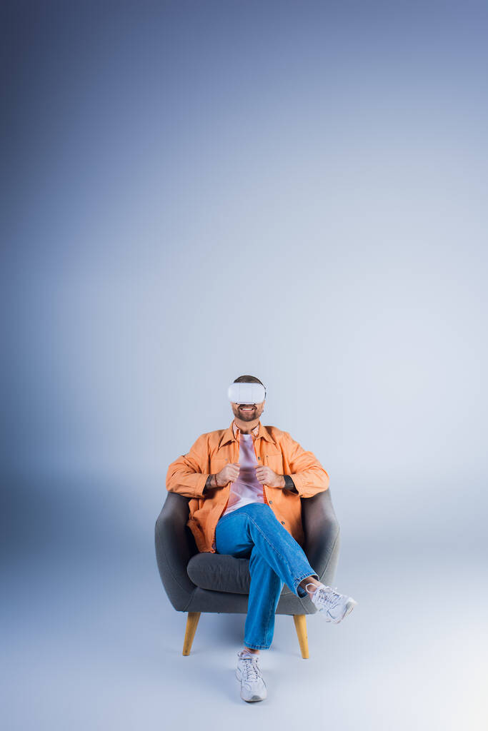 Um homem em um fone de ouvido VR confortavelmente relaxando em uma cadeira com os pés para cima em um estúdio. - Foto, Imagem