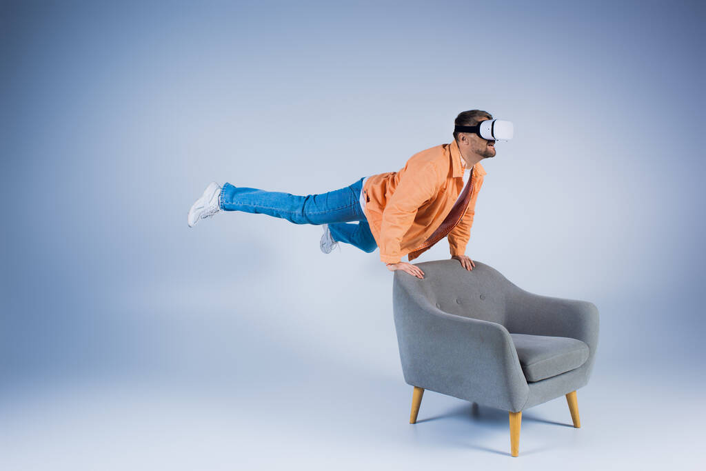 Um homem com uma camisa laranja executa um truque fascinante em uma cadeira em um estúdio, mostrando suas habilidades mágicas. - Foto, Imagem