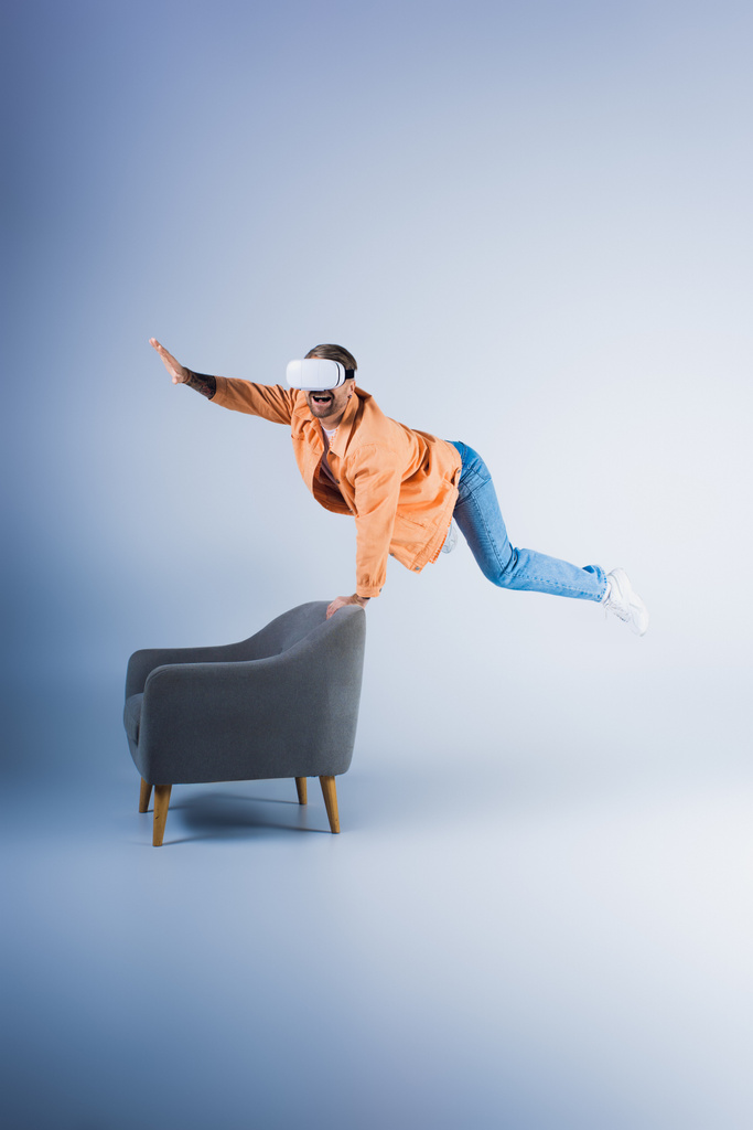 Человек в гарнитуре виртуальной реальности выполняет гравитационный трюк на стуле в футуристической студии. - Фото, изображение