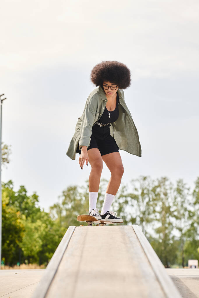 A young African American woman with curly hair skillfully rides a skateboard on a ledge at an urban skate park. - Photo, Image