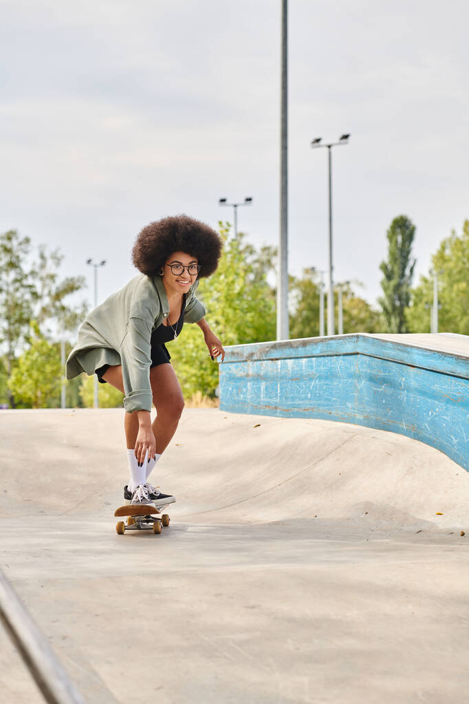 Eine junge Afroamerikanerin mit lockigem Haar skatet anmutig eine Rampe in einem Outdoor-Skatepark hinunter. - Foto, Bild