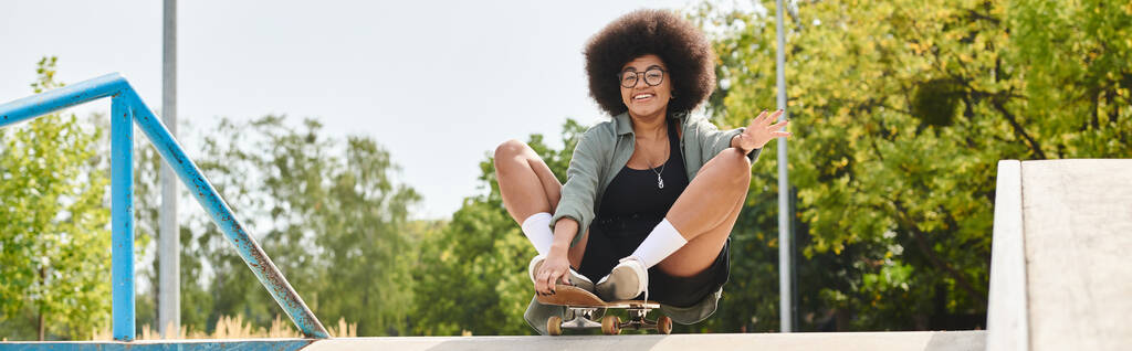 Joven mujer afroamericana con el pelo rizado disfrutando de un emocionante paseo en monopatín por una rampa en un parque de skate. - Foto, Imagen