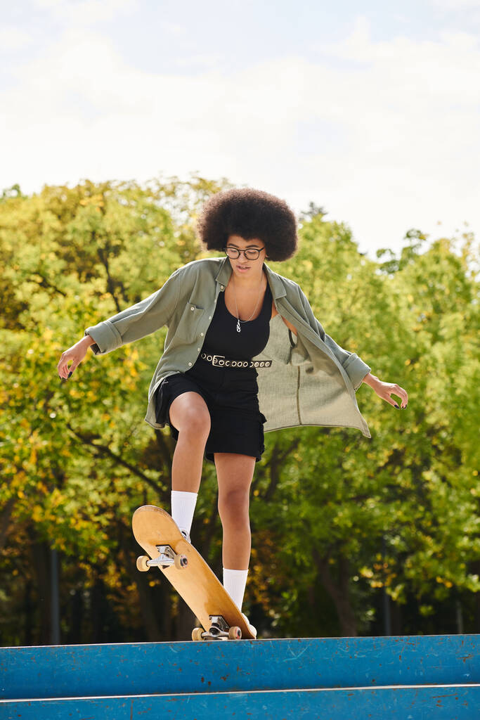 Una giovane donna afroamericana con i capelli ricci abilmente skateboard sulla cima di una rampa blu in uno skate park all'aperto. - Foto, immagini